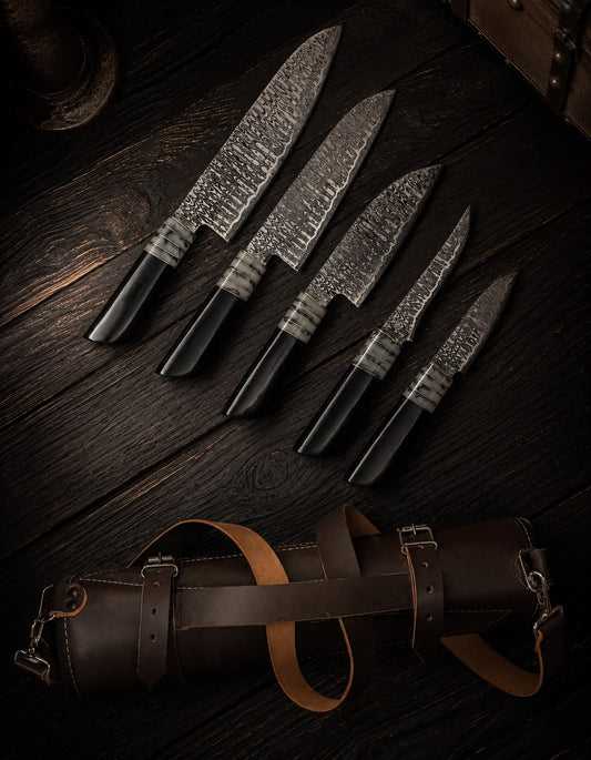 Set of four Damascus steel knives with black handles on a dark wooden surface, accompanied by a leather knife sheath.