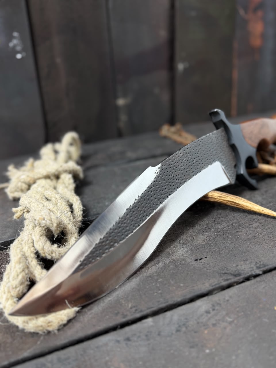 Knife with a textured handle on a wooden surface with rope and sticks.