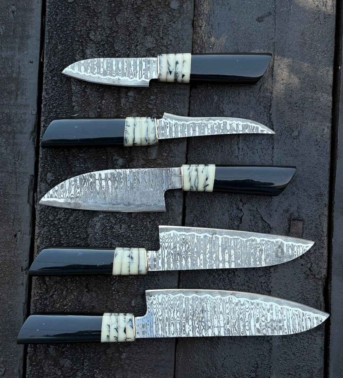 Set of five knives with black handles and silver blades on a dark surface