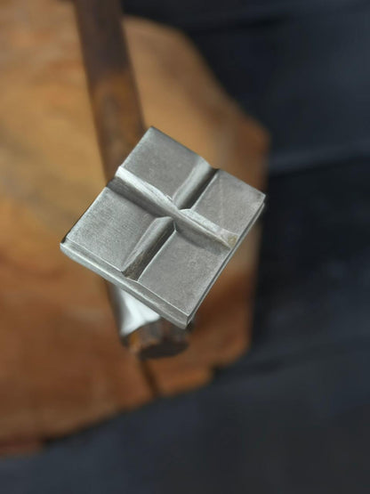 Metal stamp with a cross design on a wooden surface