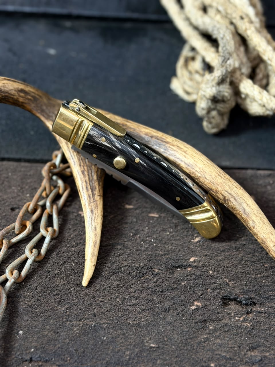 Handmade knife with wooden handle and gold accents on a dark surface with antlers and chains.