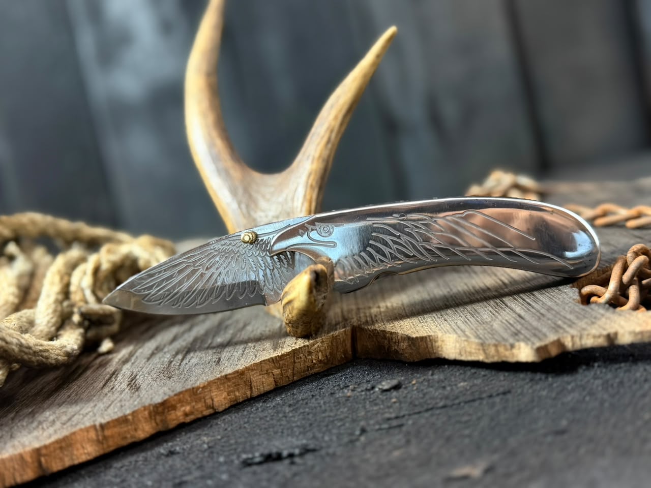 Decorative knife with engraved design on a wooden surface with antlers and rope.