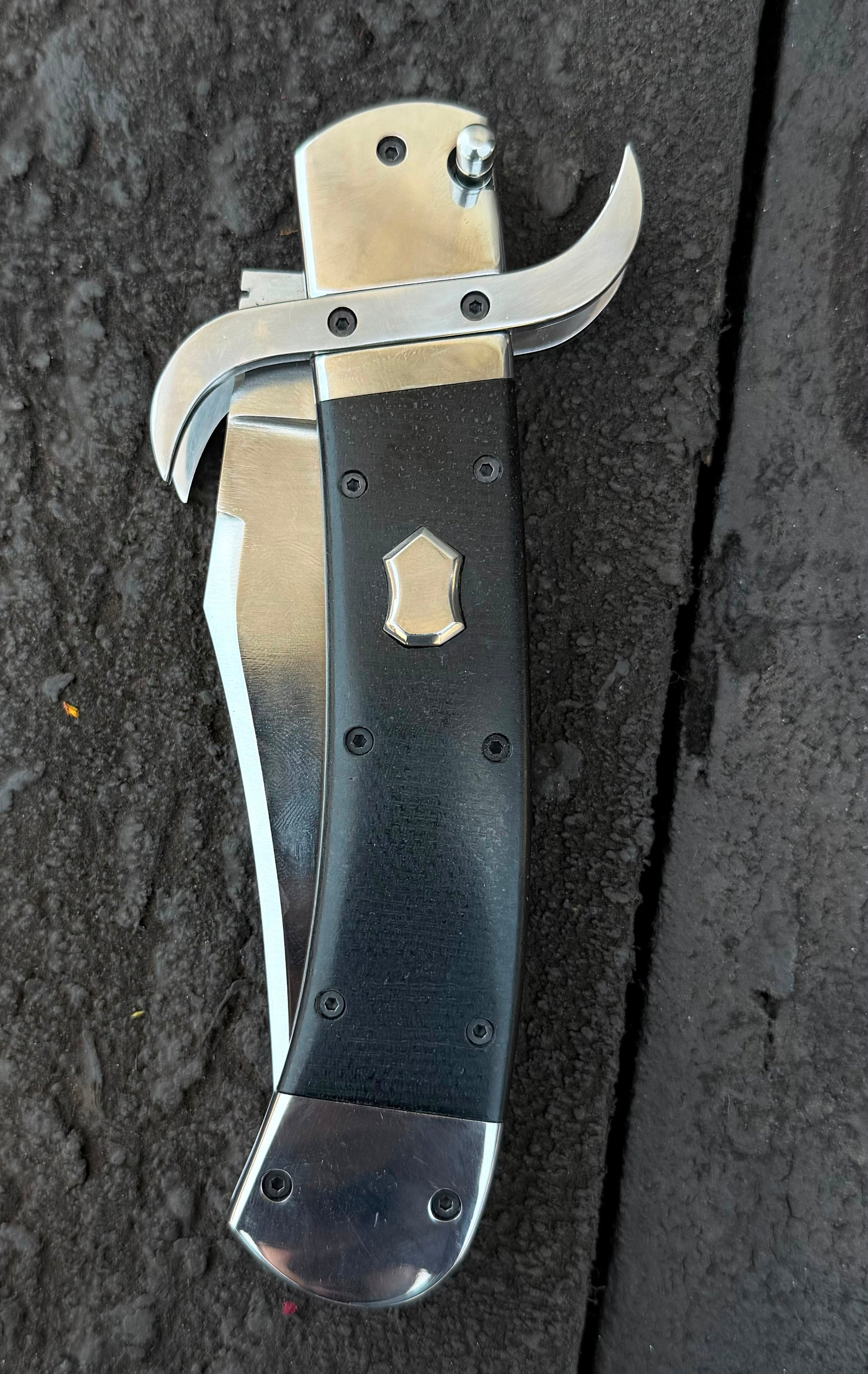 Folded knife with a black handle and silver blade on a dark textured surface