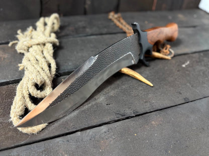 Knife with a textured black handle and blade on a wooden surface with rope and wood pieces.