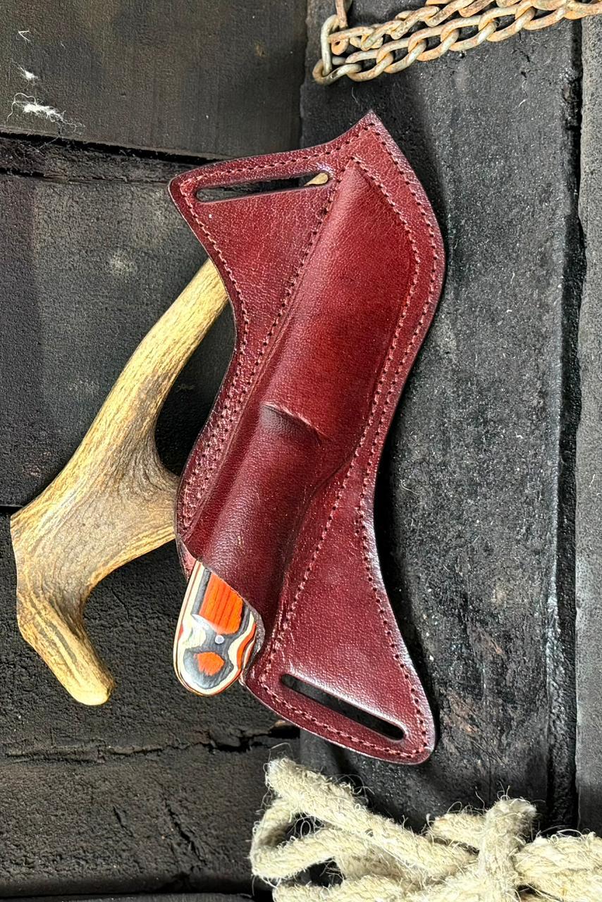 Red leather knife sheath with a visible brand logo on a dark stone background