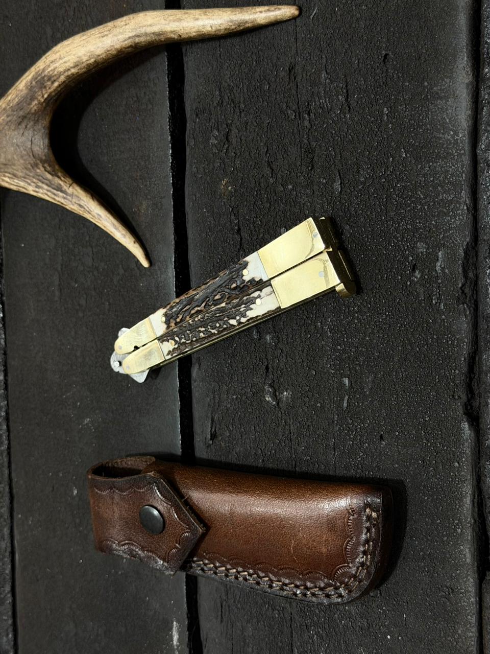 Knife with staghorn handle and leather sheath on a dark surface