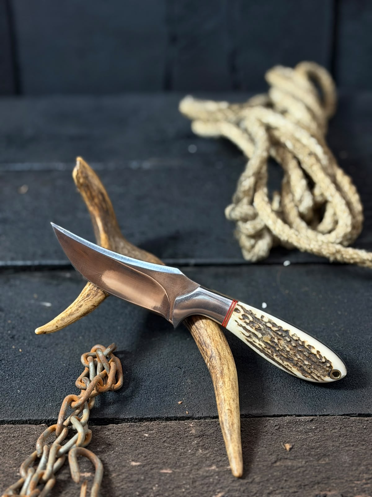 Knife with wooden handle on a dark surface with antlers and rope
