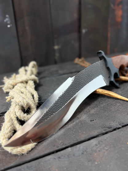 Knife with a textured handle on a wooden surface with rope and sticks.