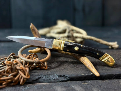Decorative knife with gold handle and black blade on a dark surface with chains.
