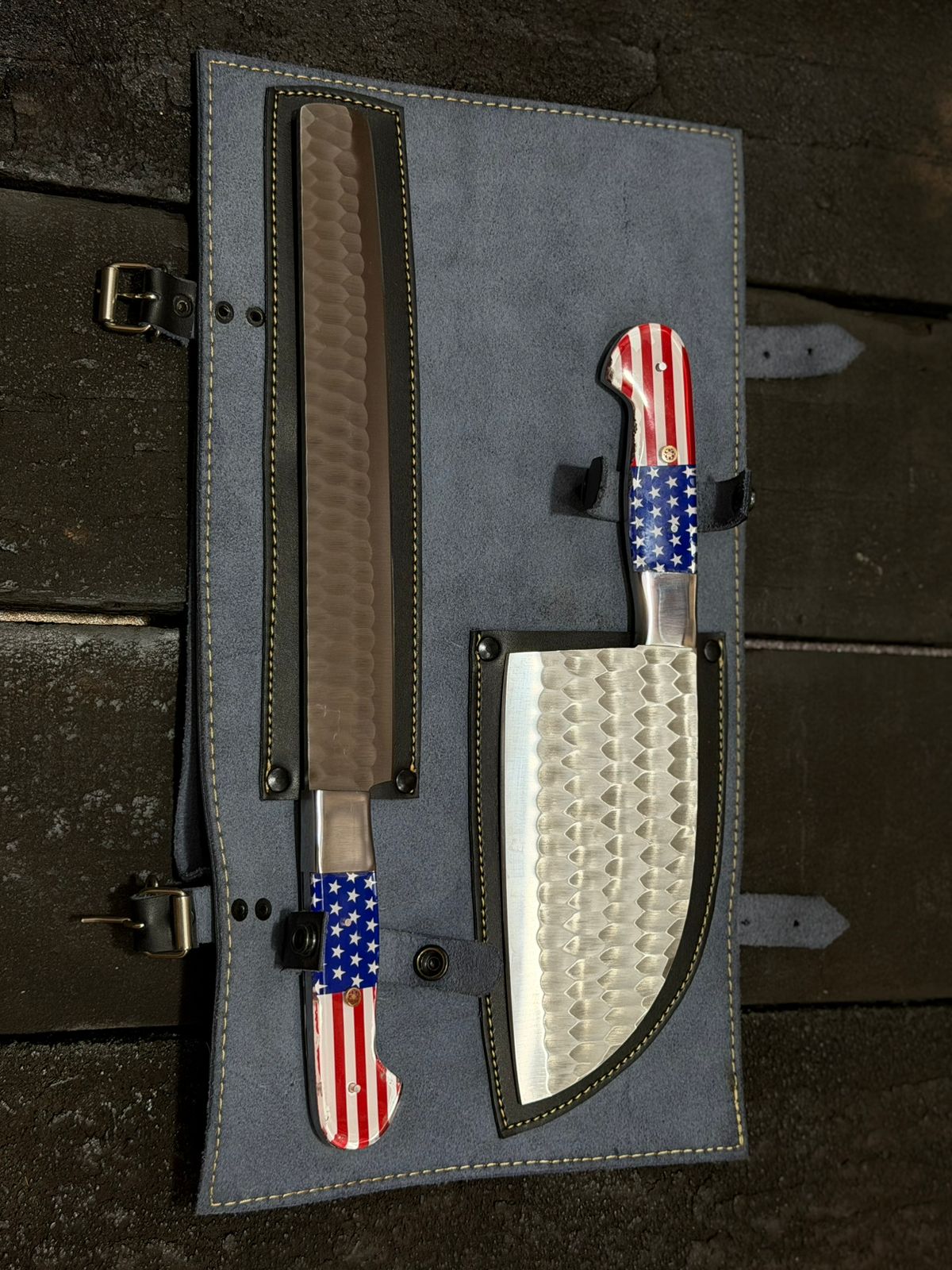 Set of knives with American flag patterns in a gray leather sheath on a dark wooden surface.