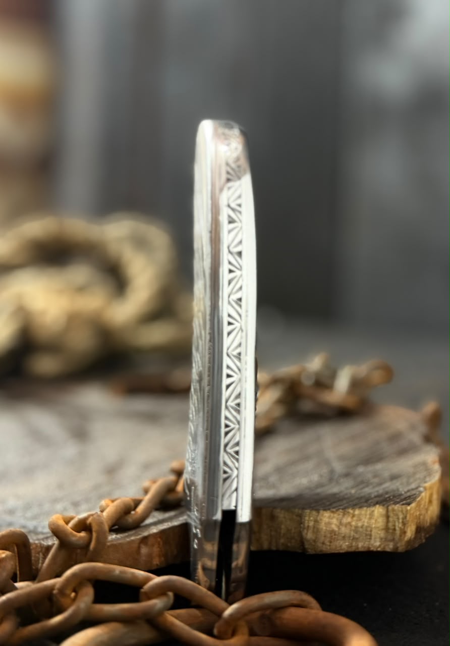 Decorative metal blade with intricate patterns on a wooden block and chain background
