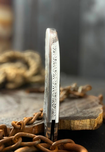 Decorative metal blade with intricate patterns on a wooden block and chain background