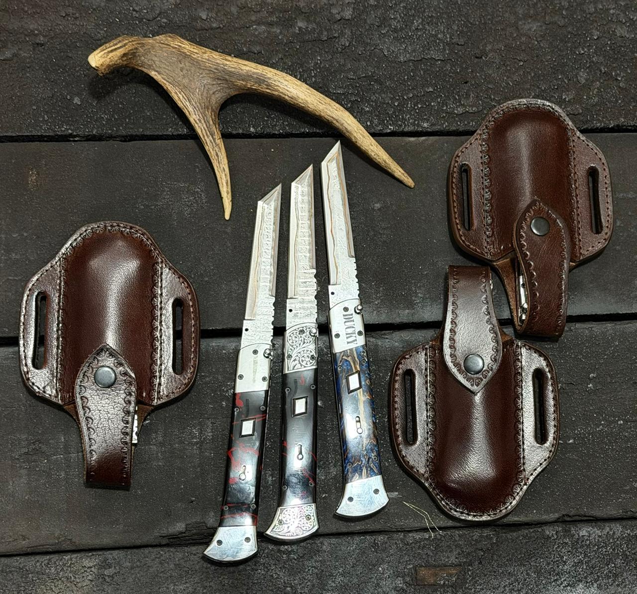 Three knives with leather sheaths and a deer antler on a wooden surface