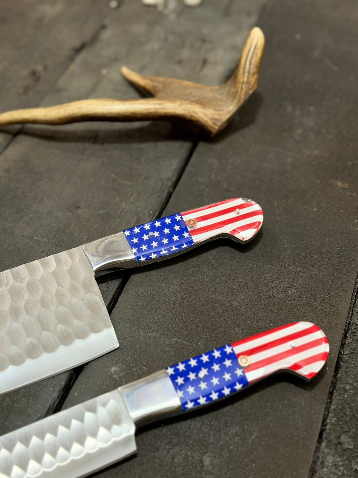 Two pocket knives with American flag handles on a dark surface.