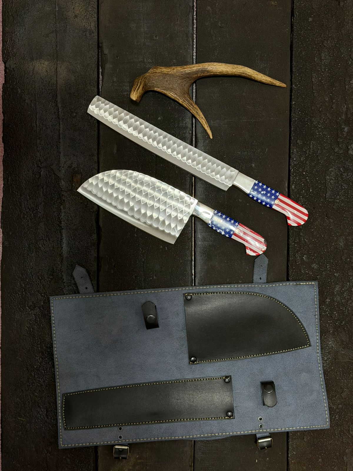 Two knives with American flag design and a black leather sheath on a dark wooden surface.