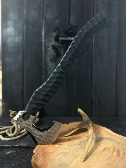 Tomahawk with a black handle on a wooden surface with a dark background 