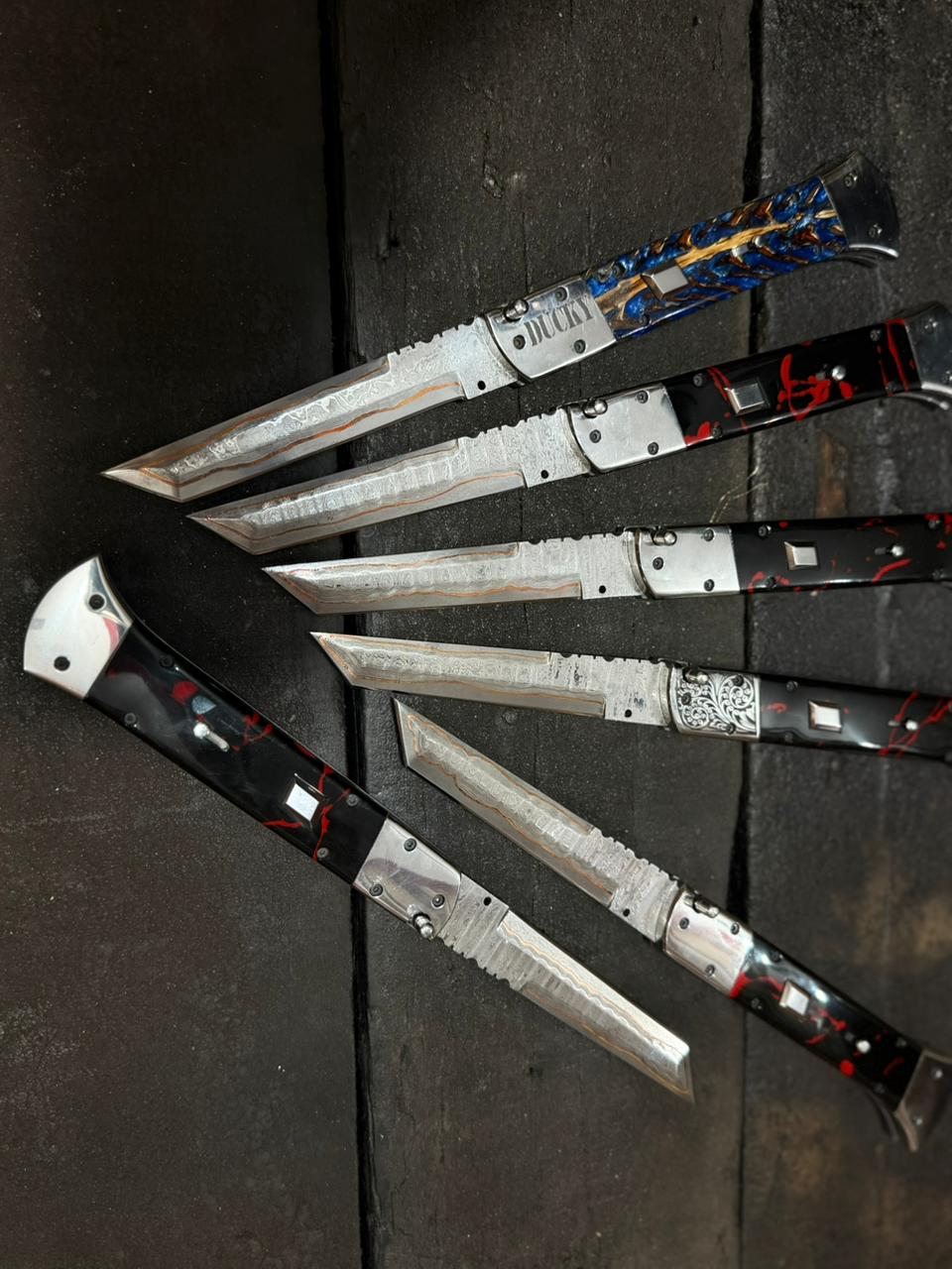 Set of folding knives with metallic blades and black handles on a dark surface