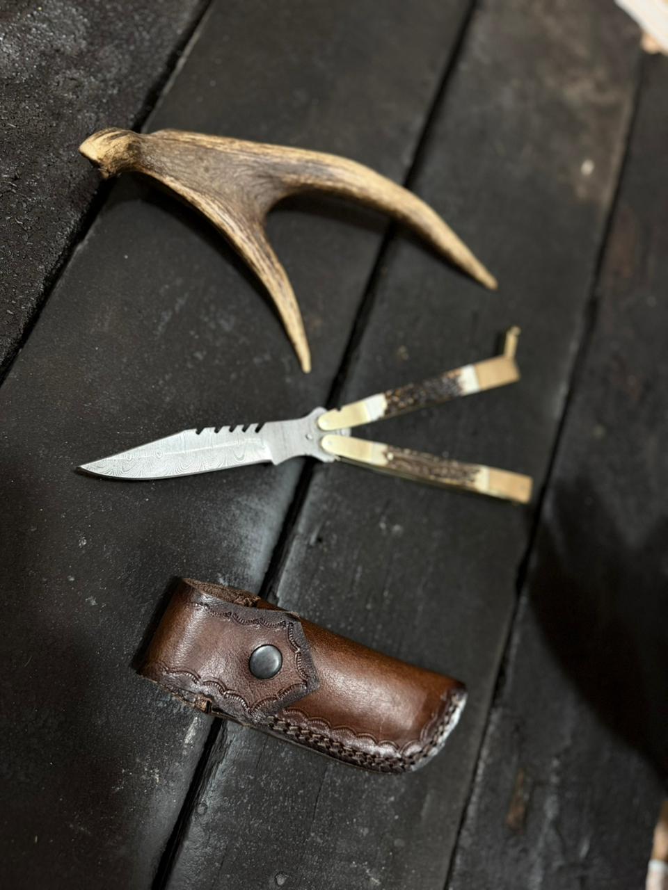Knife with leather sheath and deer antler on dark wooden surface