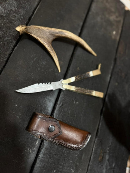 Knife with leather sheath and deer antler on dark wooden surface