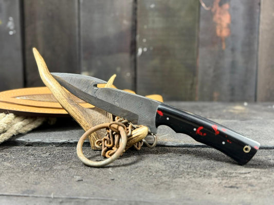 Damascus Knife with black handle and red accents attached to a wooden surface