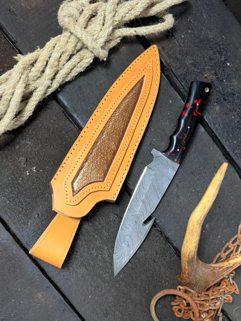 Hunting Knife with a leather sheath on a dark surface with rope and antlers.