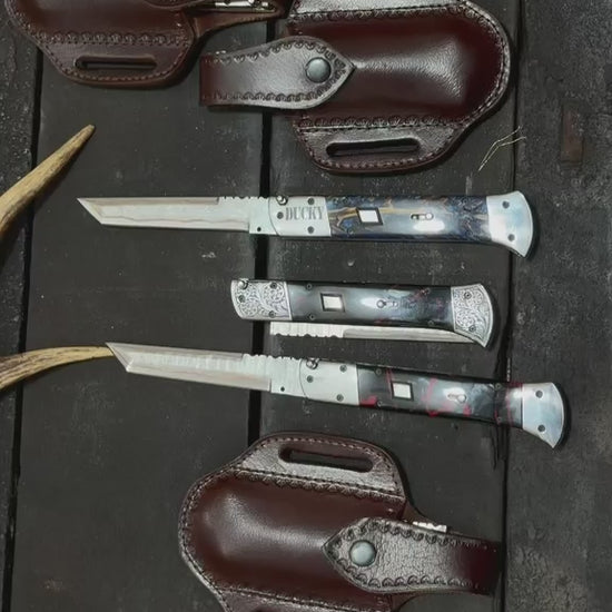 Handmade automatic switchblade knives with Damascus steel blades and custom engraved bolsters on rustic wooden background
