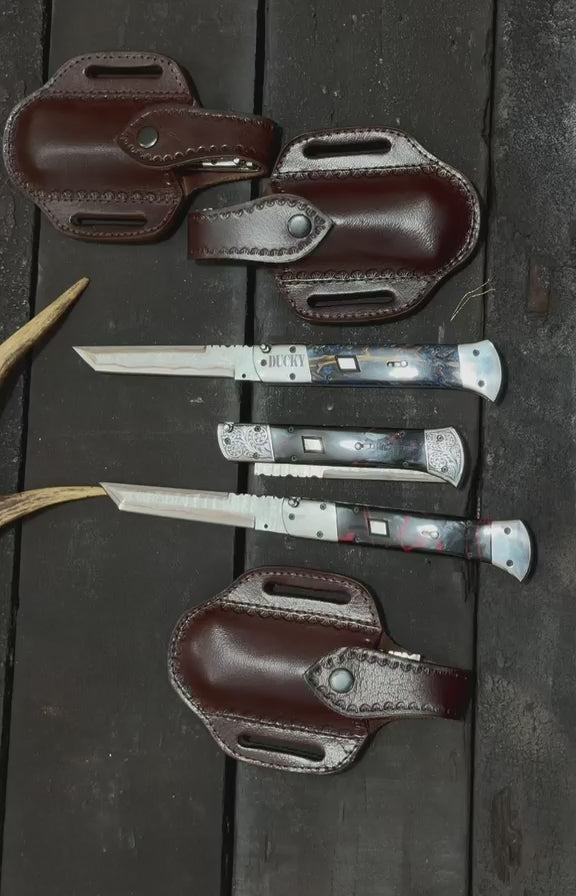 Handmade automatic switchblade knives with Damascus steel blades and custom engraved bolsters on rustic wooden background